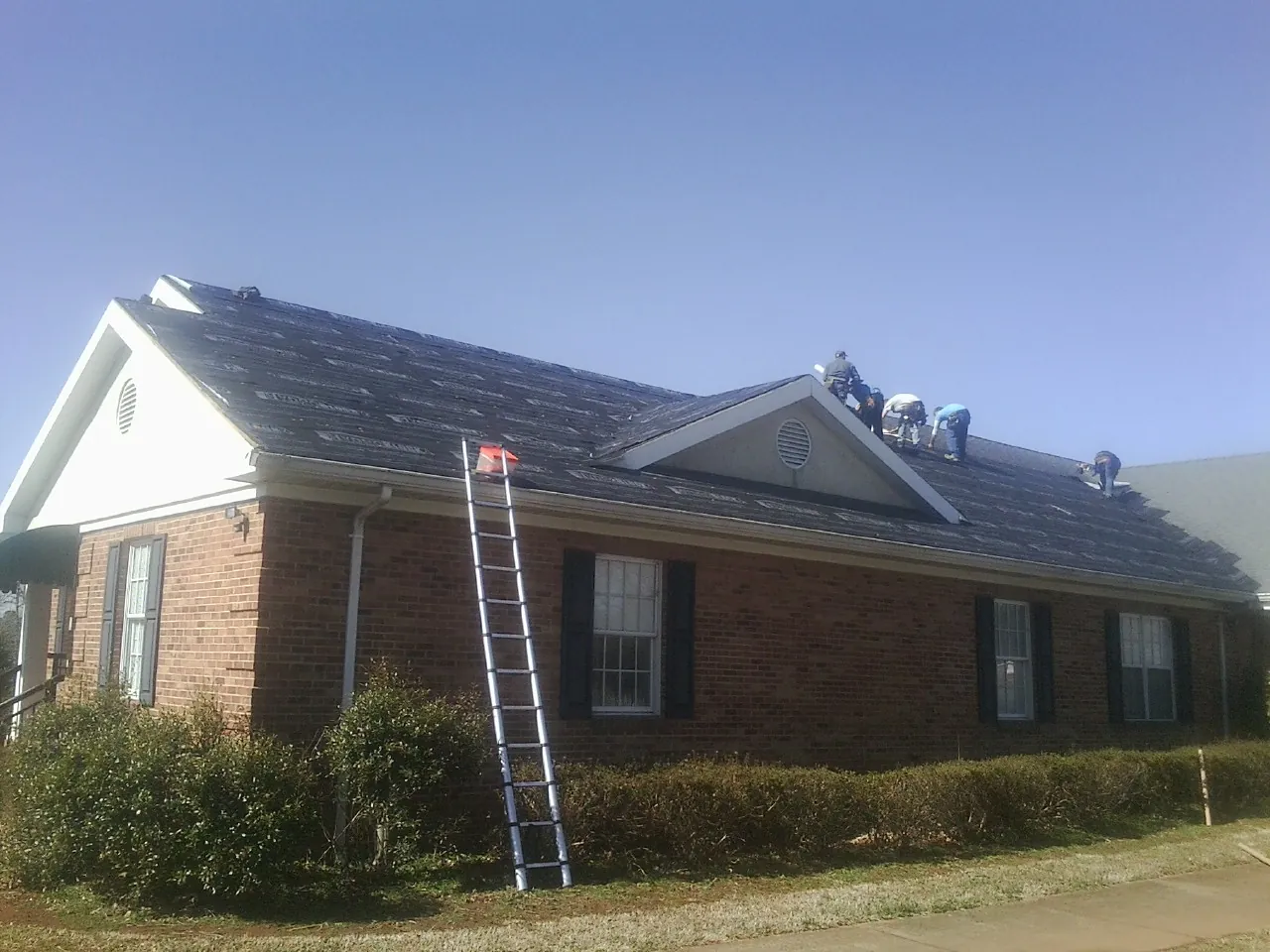 Crew tearing shingles off a brick ranch roof with a ladder set — Emergency Roof Repair work by our crew in Eastport