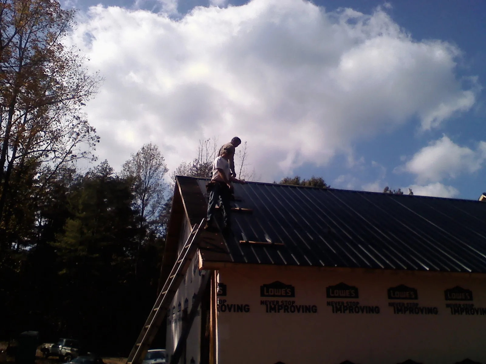 Roofer fastening dark metal panels high against a cloudy sky, from a Roof Inspection job in Eastport